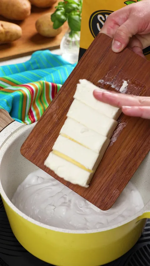 A block of cream cheese, cut into pieces, sliding off a wooden board into the coconut milk.