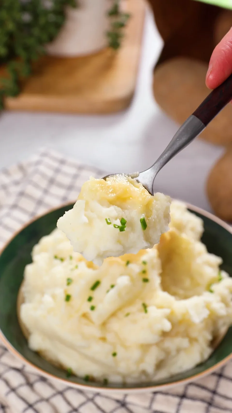 A spoonful of mashed potatoes with a smear of miso butter and chives, lifted above the bowl.