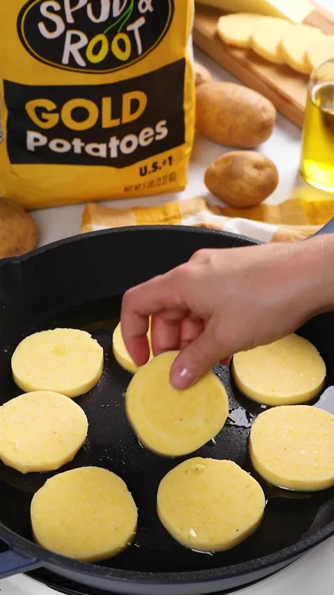 A hand laying pale polenta rounds into the oiled skillet.