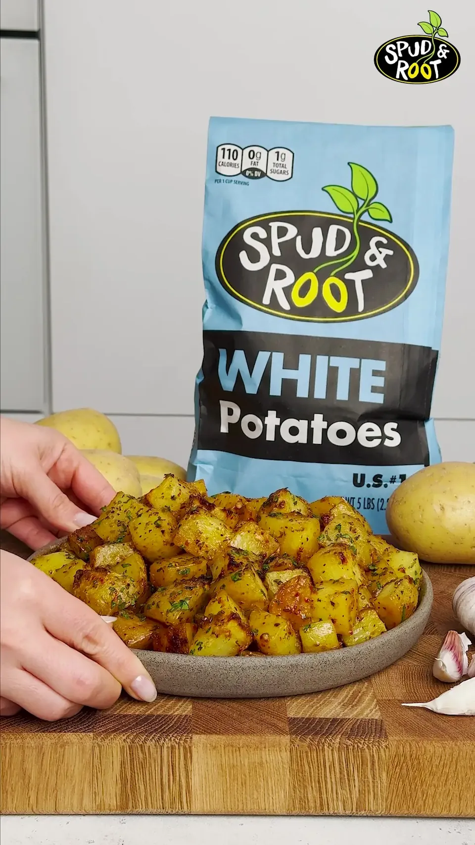 A plate of golden roasted potato cubes in front of a bag of Spud & Root White Potatoes.