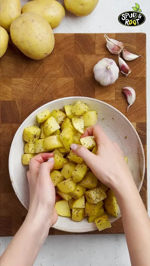 Two hands tossing the potato cubes in the bowl to coat them.