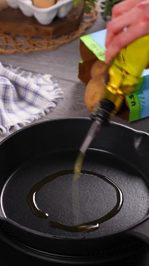 Olive oil being poured in a ring into an empty cast-iron skillet.